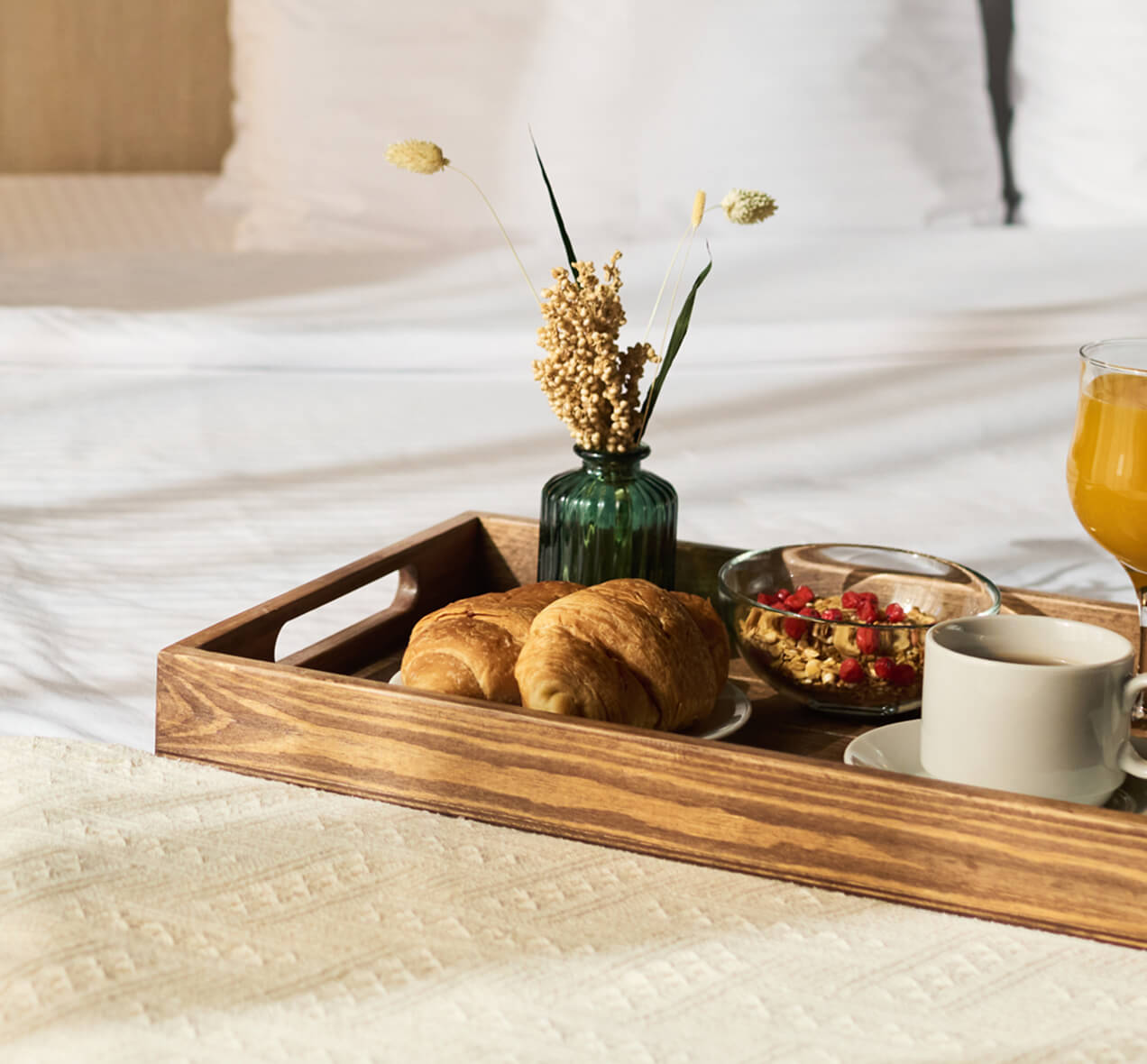 Wooden tray with pastries, coffee, and fruit on a bed