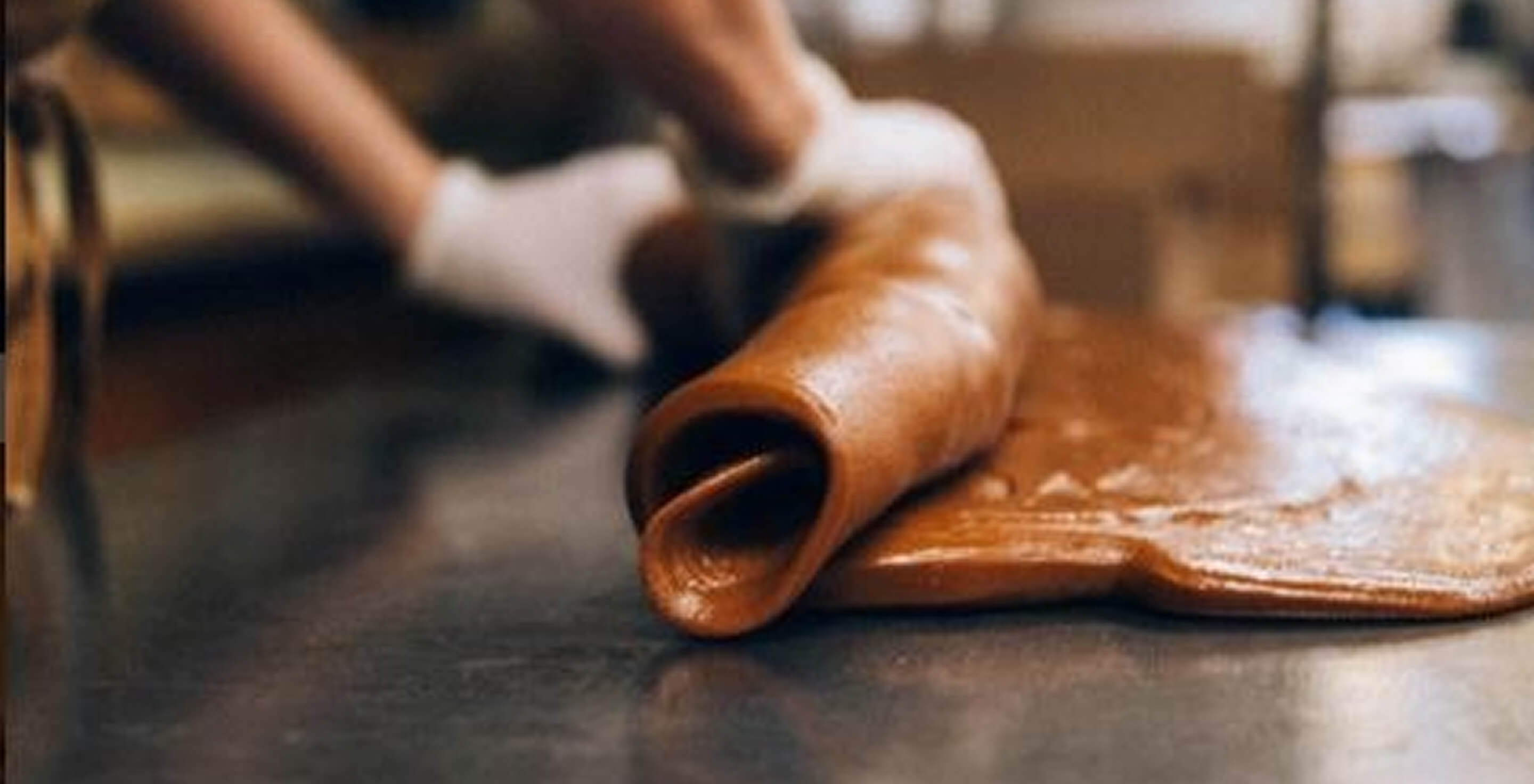 Person rolling out a large sheet of caramel on a countertop.